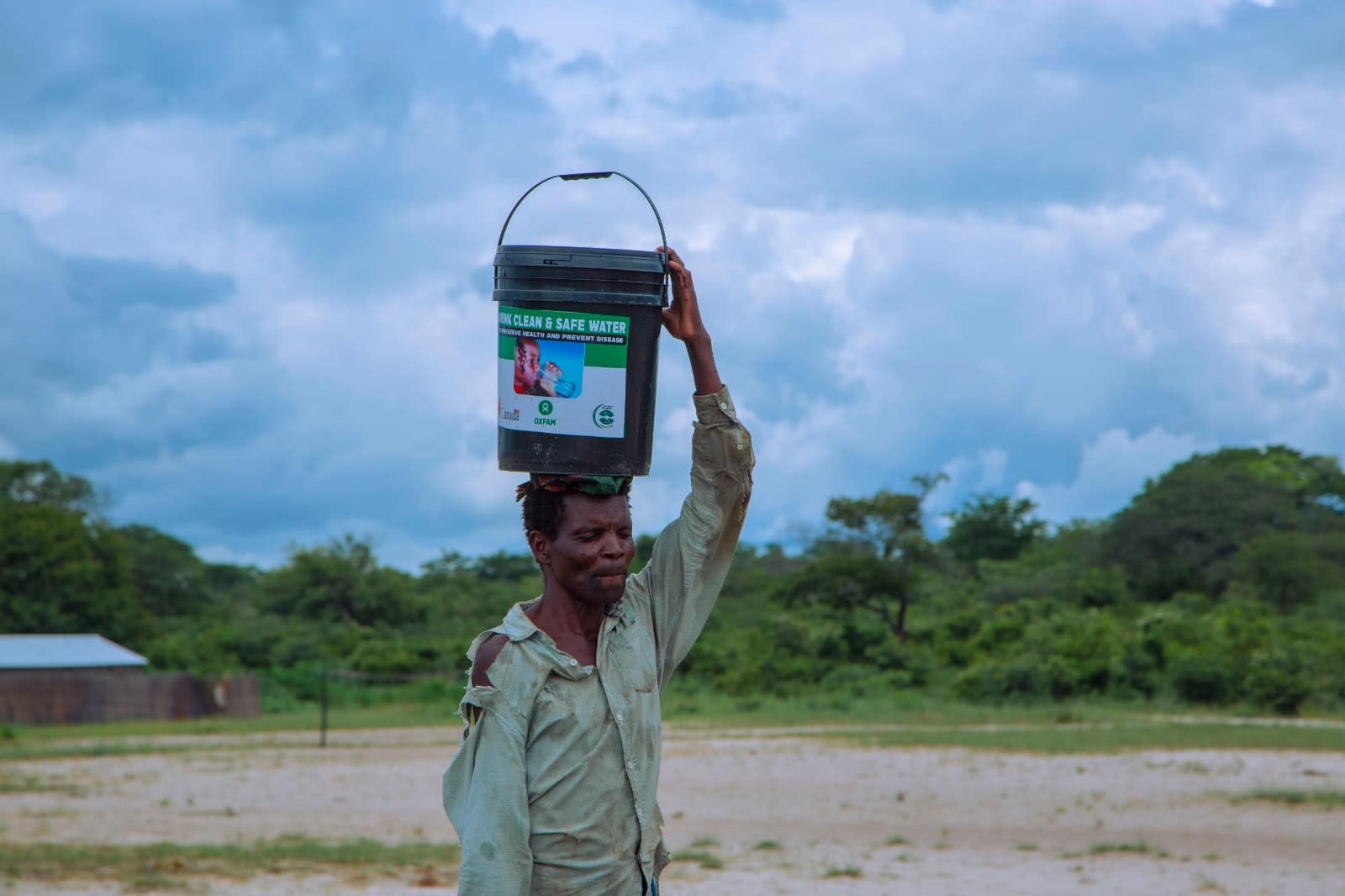 Man carrying a bucket of safe drinking water provided through a drought response project in rural Zambia